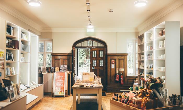 Brightly lit and well stocked gift shop with shelving units on either side and two display tables in the centre and foreground.